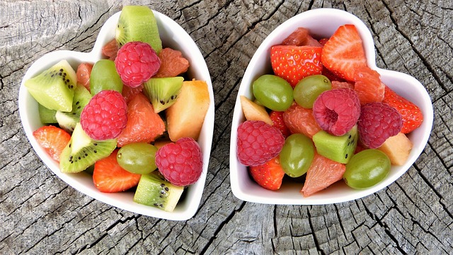 Miseczki w kształcie serca z kolorowymi owocami: truskawkami, malinami, kiwi, winogronami, bananami, grejpfrutem i melonem